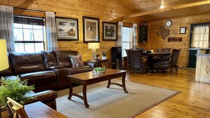 A cozy living room with a leather sofa, a wooden coffee table, and a dining area with a table and chairs. - Once a Part of the Beloved Shady Oak Lodge - Cabin 1 - 4 beds with Boat Ramp (Many)