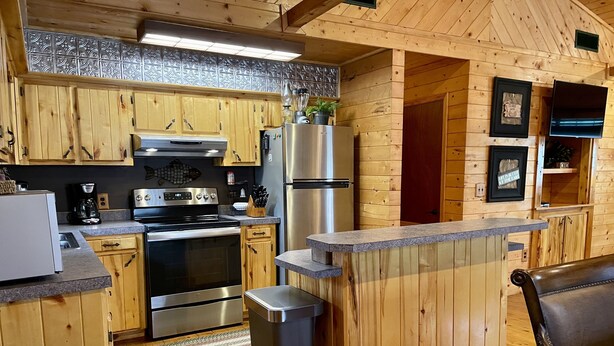 A compact kitchen with wooden cabinets, stainless steel appliances, and a small island counter. - Once a Part of the Beloved Shady Oak Lodge - Cabin 1 - 4 beds with Boat Ramp (Many)