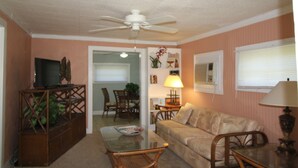 A living room with a glass coffee table, a beige sofa, a wooden cabinet, and a ceiling fan.