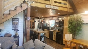 Interior acogedor de una cabaña con una escalera de madera, una zona de cocina con electrodomésticos modernos, una mesa de comedor y un área de estar confortable.