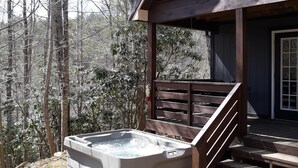 Una cabaña de madera con un jacuzzi y escalones de piedra que llevan a un porche.
