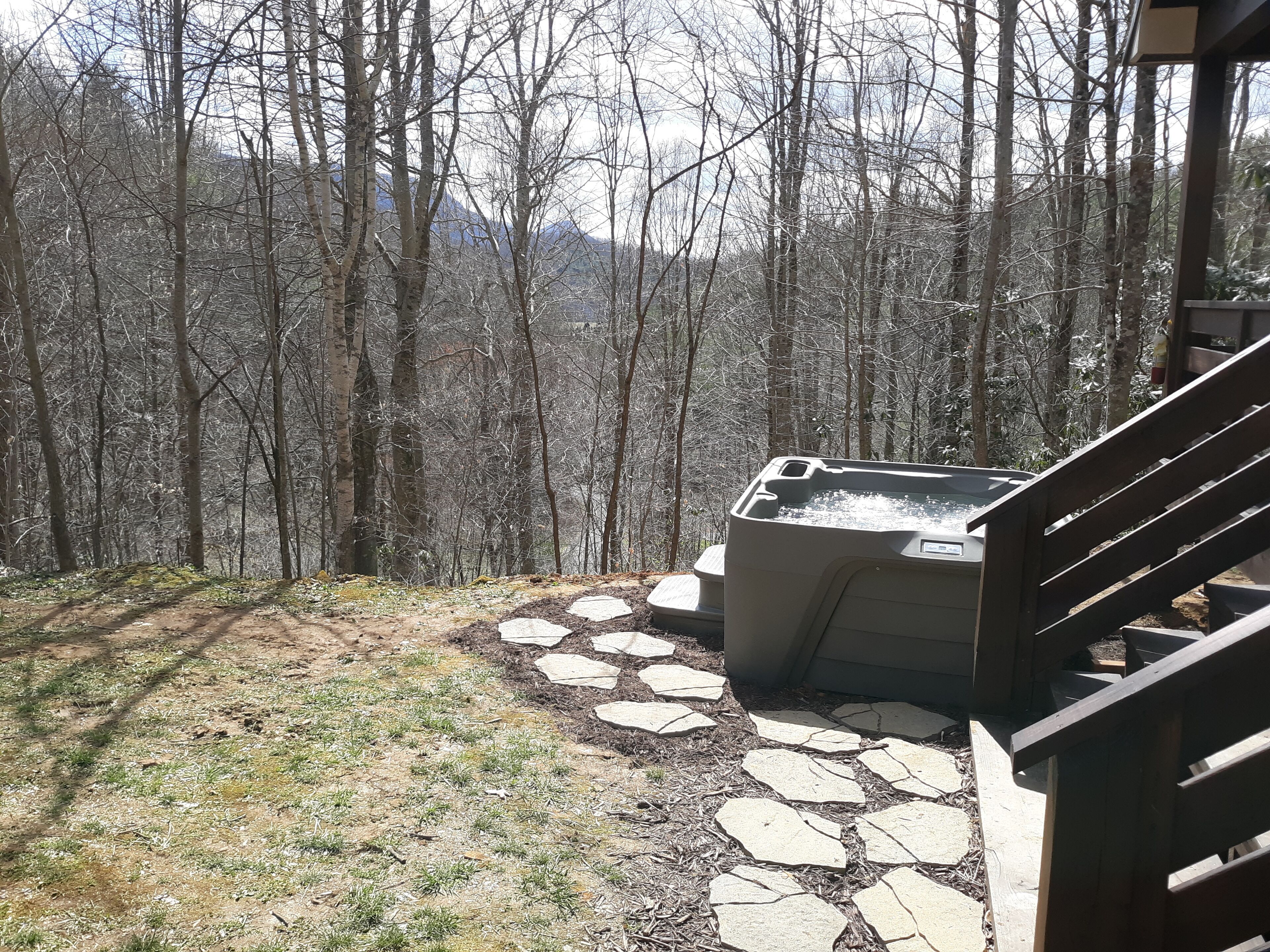 Un jacuzzi en un área boscosa, con un camino de piedra que lo conduce.
