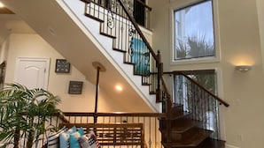 Un interior espacioso con una escalera de madera, un ventanal grande y un banco con cojines.