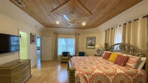 Un dormitorio con techo de madera, una cama con ropa de cama estampada, un televisor, un aparador y una silla.