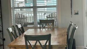 Een eetgedeelte met een houten tafel en stoelen, een plafondventilator en een raam met jaloezieën.