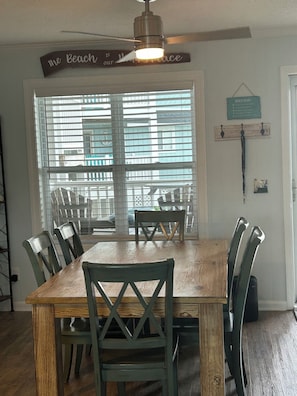 A dining area with a wooden table and chairs, a ceiling fan, and a window with blinds.