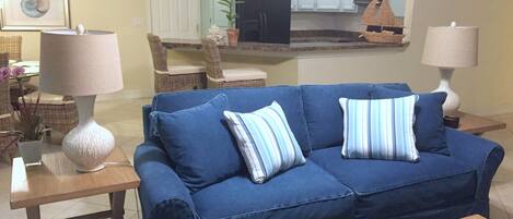A living room with a blue sofa, two lamps, a remote control, and a small decorative item on a wooden coffee table.