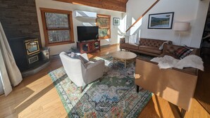 A cozy living room with a fireplace, a television, a sofa, and a coffee table. - 5BR Catskills Retreat • Ski Close • Hot Tub, Firepit, 2 grills, Deck, Fast WiFi (Prattsville)