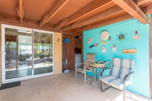 A covered outdoor area with a sliding glass door leading to a patio, a blue wall with various decorations, a striped chair, and a small table. - DESERT OASIS FOR RELAXING (Tucson)