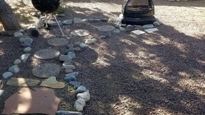 Un jardin avec un barbecue, un foyer et un chemin en pierre.