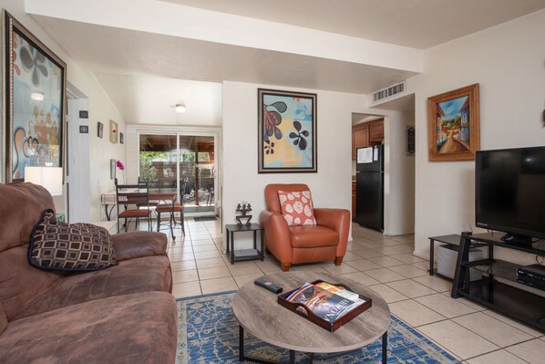 A living room with a brown leather sofa, a coffee table with a magazine, a TV on a stand, and a painting on the wall. - DESERT OASIS FOR RELAXING (Tucson)
