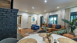 A modern living room with a fireplace, a dining area with a round table, and a kitchen in the background. - Casa Boheme-Stylish, Relaxing, Close to Downtown! (Guerneville)