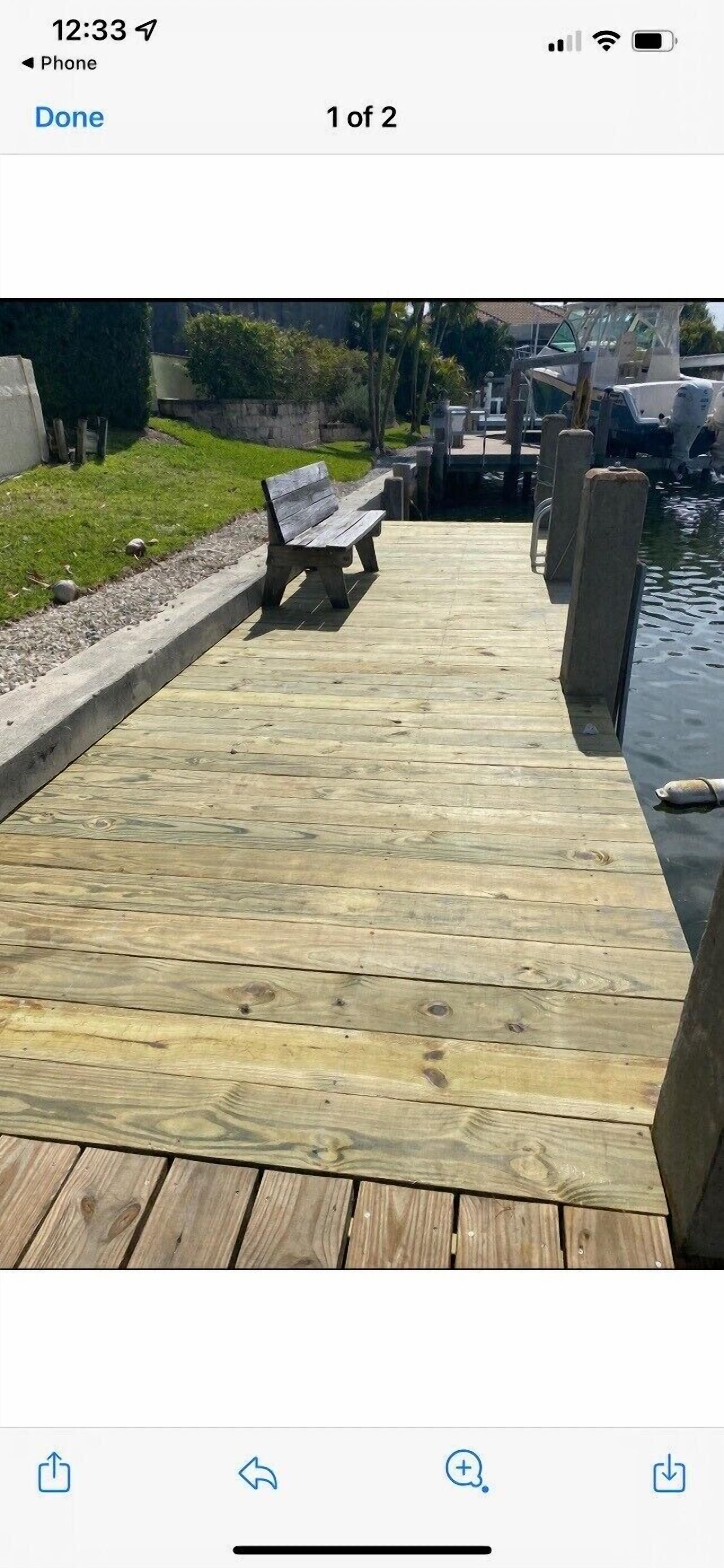 A wooden dock with a bench, leading to a body of water with boats.