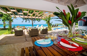 A wooden table set for dining with a view of the ocean and lounge chairs under a pergola. - Seahorse- - A Slice Of Caribbean Paradise On A Private Beach, Gated Community (Rio Bueno)