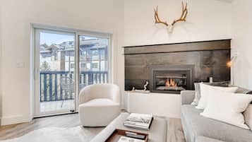 A modern living room with a fireplace, a sofa, a chair, and a view of a balcony with a railing.