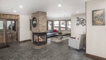 A modern living room with a stone fireplace, a grey sofa, and a large window offering a view of the outdoors.