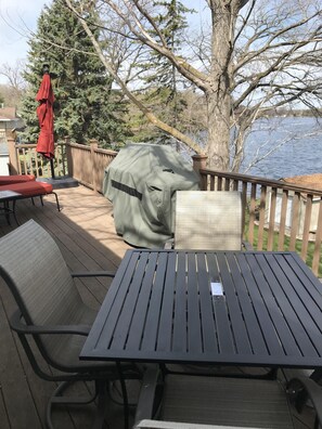 Una terraza con parrilla cubierta, mobiliario exterior y vista a un lago.