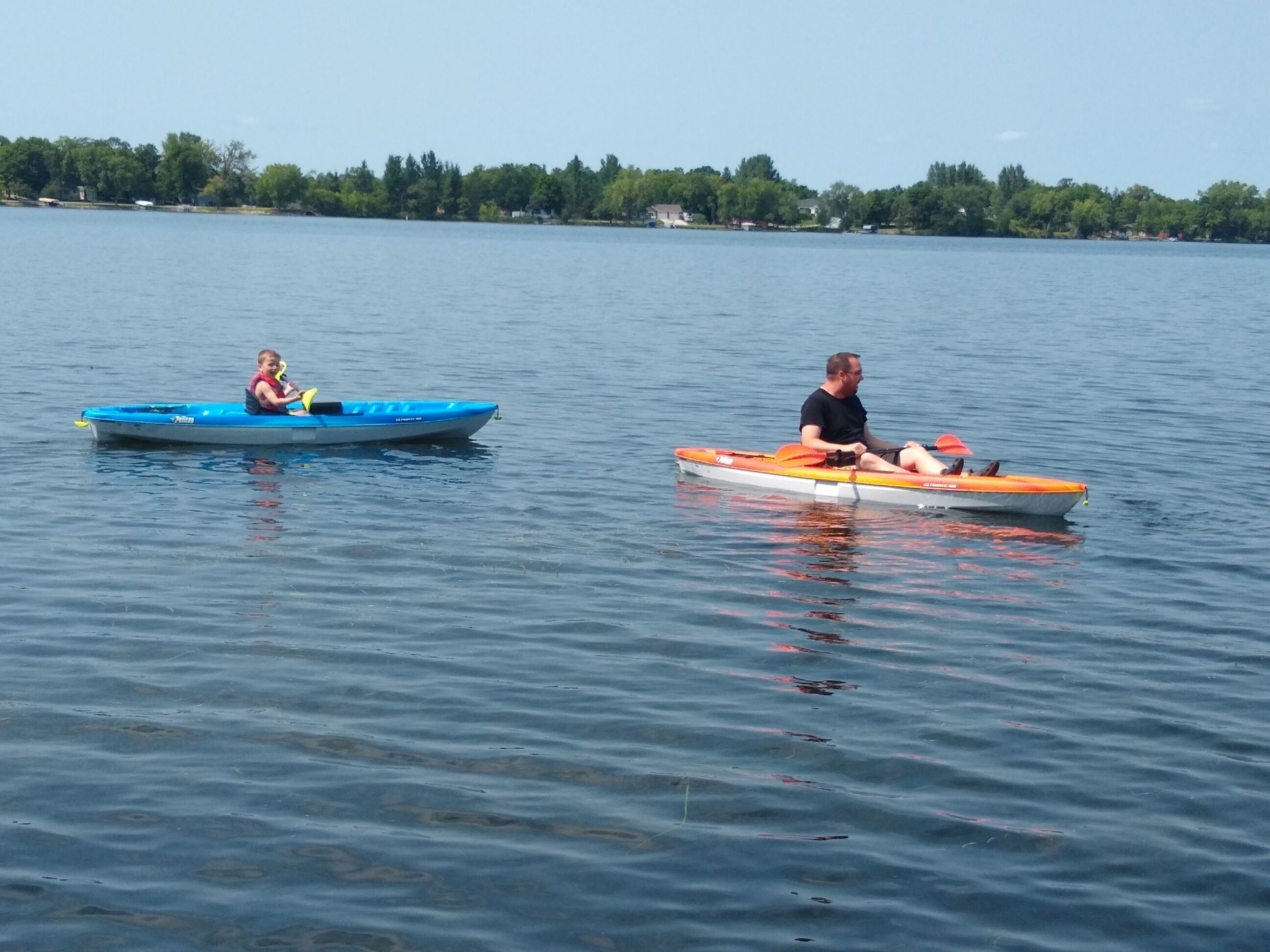 Deux bateaux sur un lac paisible, avec une rive boisée en arrière-plan.