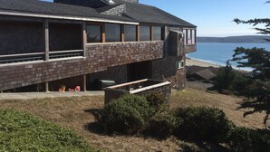 Un bâtiment moderne à deux étages, doté de grandes fenêtres et d’un toit en pente, qui offre une vue sur une plage.
