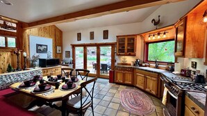 A kitchen with wooden cabinets, a dining area with a table set for four, and a large window providing natural light. - Peaceful Pines "  Lovely Pet Friendly Mountain Home w/ Spa (Idyllwild)