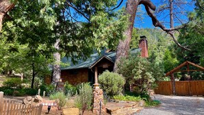 A rustic cabin with a stone chimney, surrounded by dense trees and a wooden fence. - Peaceful Pines "  Lovely Pet Friendly Mountain Home w/ Spa (Idyllwild)