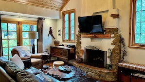 A cozy living room with a stone fireplace, leather sofa, and a flat-screen TV mounted above it. - Peaceful Pines "  Lovely Pet Friendly Mountain Home w/ Spa (Idyllwild)