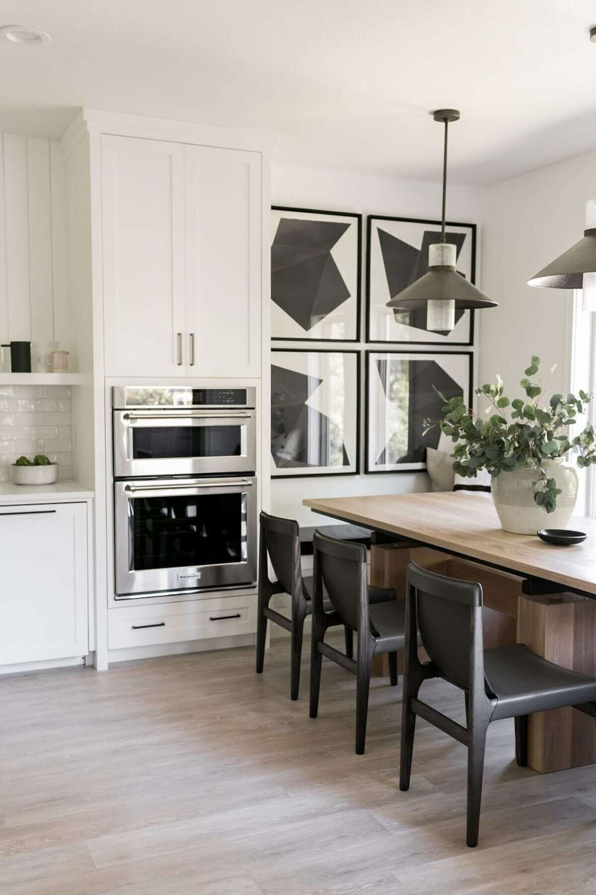 A modern kitchen with white cabinets, stainless steel appliances, a wooden dining table, and a potted plant.