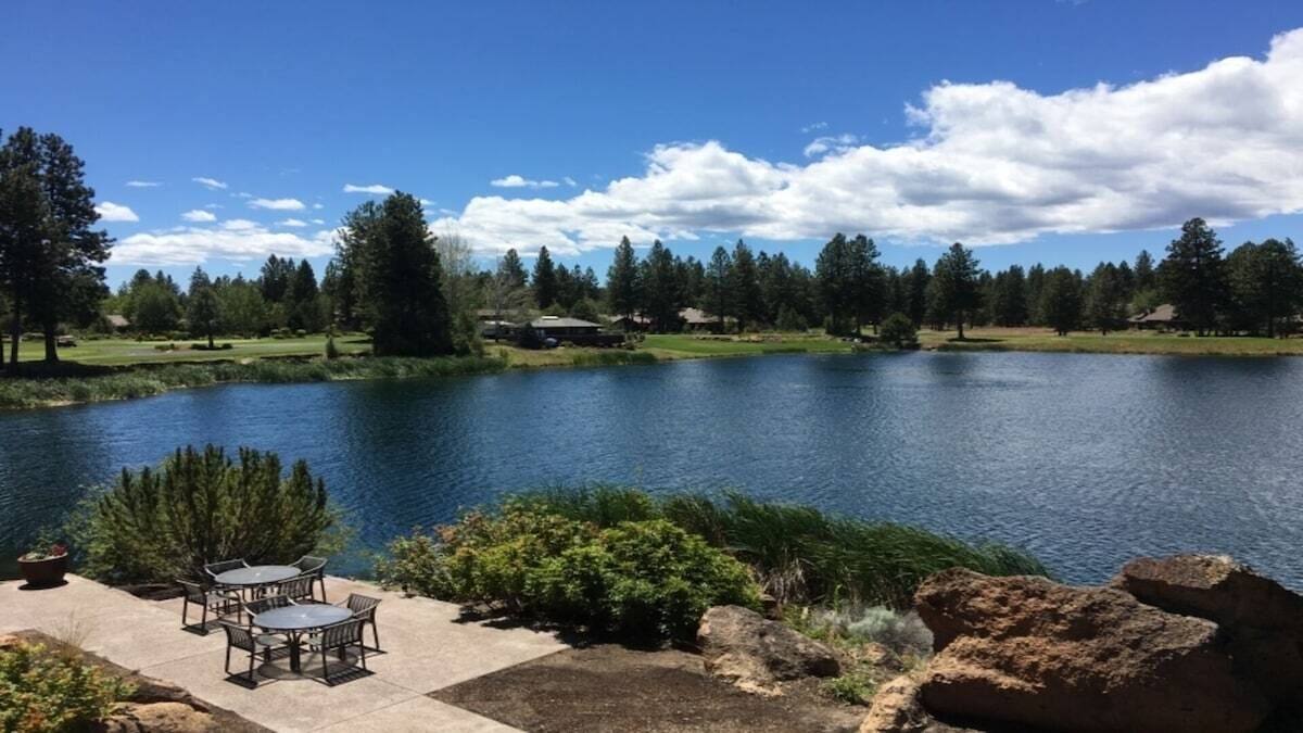 A lakeside patio with outdoor furniture and a view of the lake and surrounding trees.