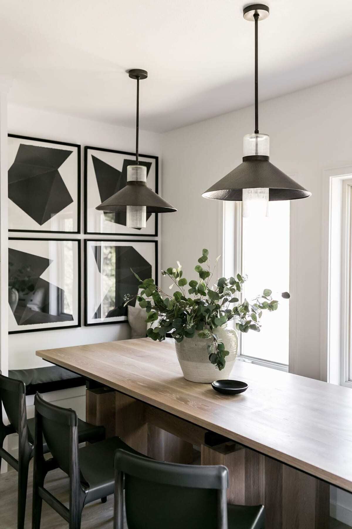 A modern kitchen with a wooden island, black chairs, and pendant lights.