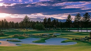 Um campo de golfe com vários bunkers, obstáculos de água e um cenário de árvores e montanhas ao longe.