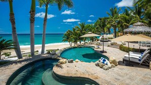 Un espace piscine avec des chaises longues, un parasol en chaume et une vue sur la plage.