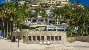 Un hôtel situé sur la côte, avec plusieurs étages, une architecture en pierre et des palmiers.