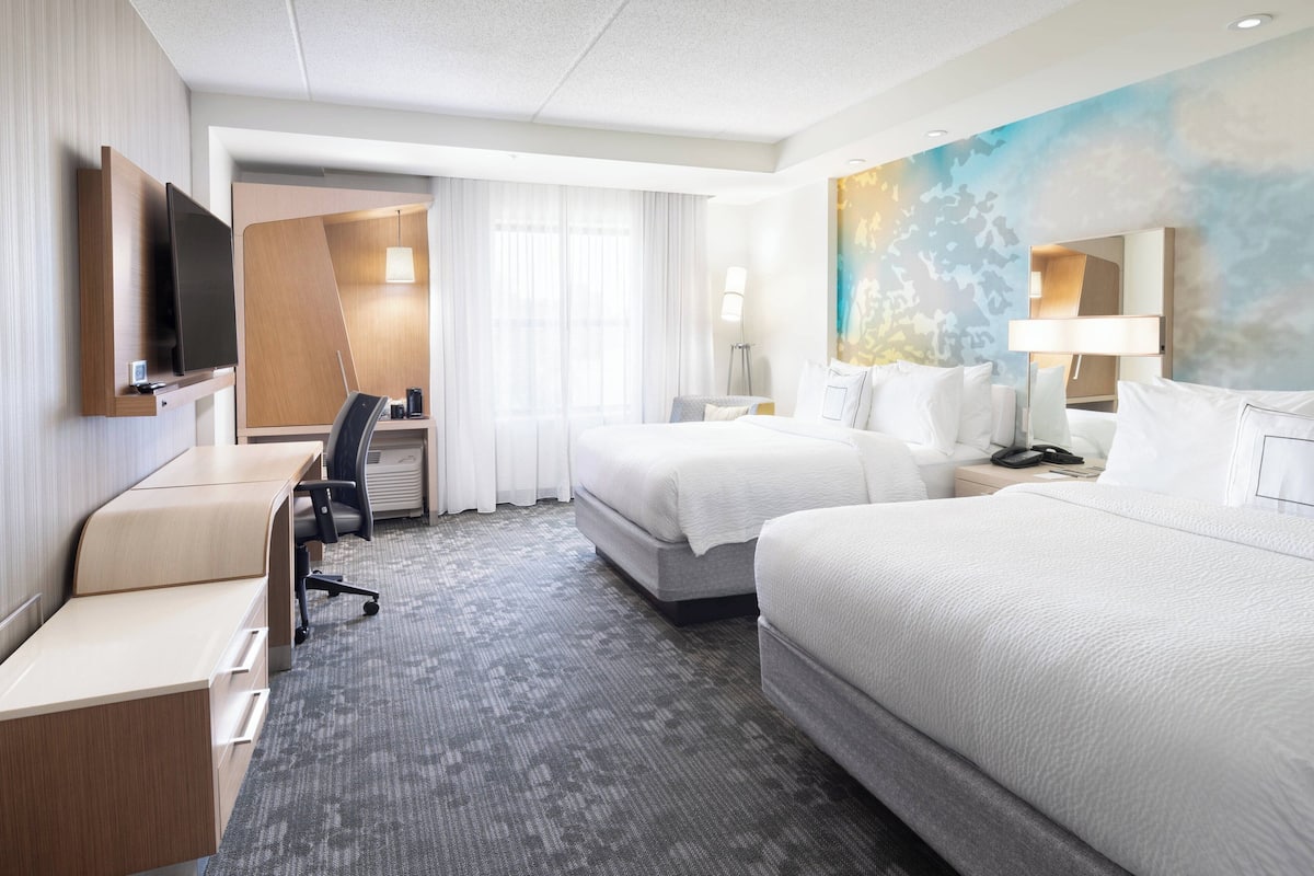 A hotel room with a bed, a desk, a chair, a TV, and a painting on the wall.