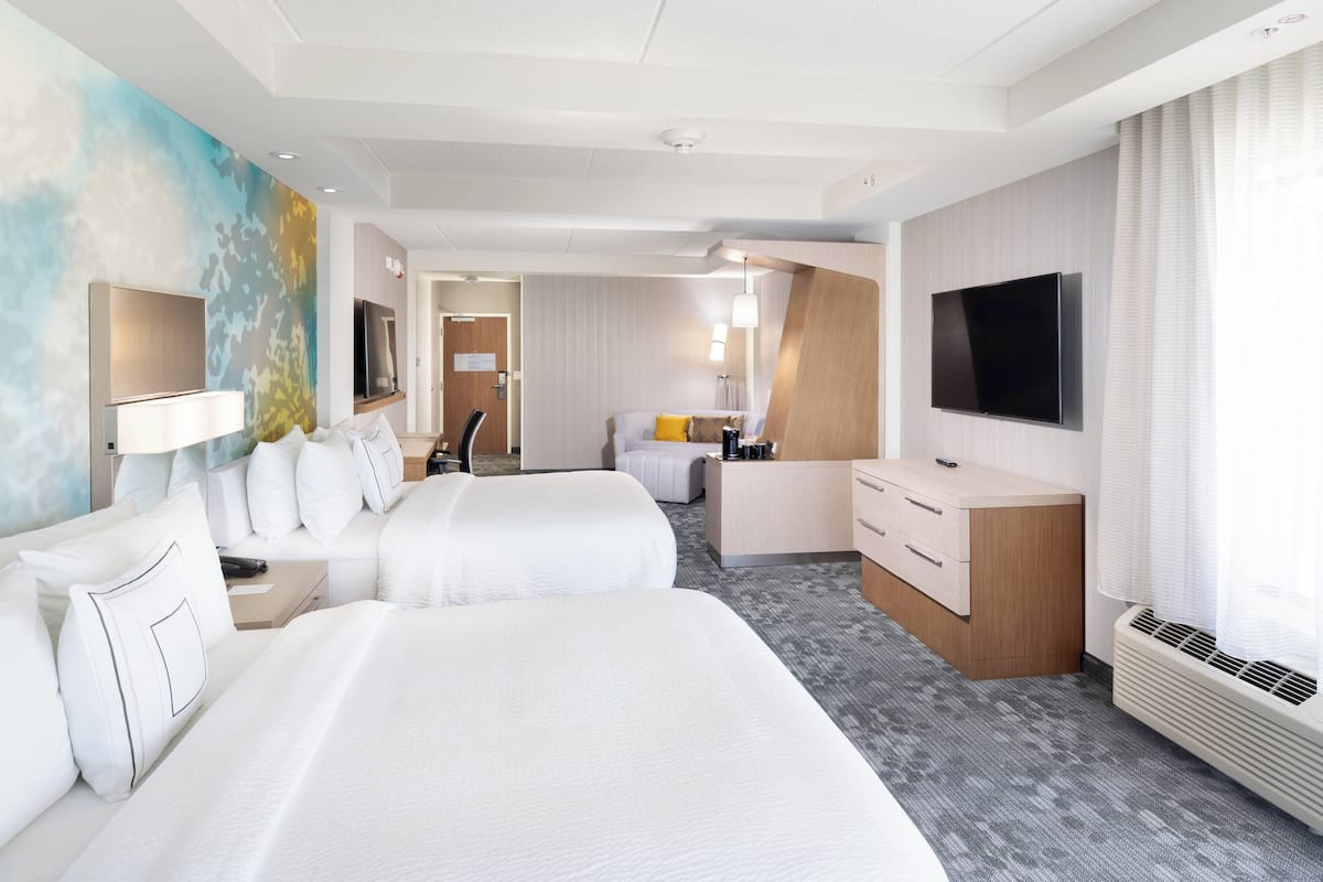A hotel room with two beds, a desk, a TV, and a bathroom.