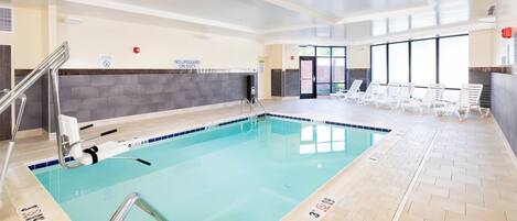 En indendørs swimmingpool med klart vand, en redningsstation og liggestole.