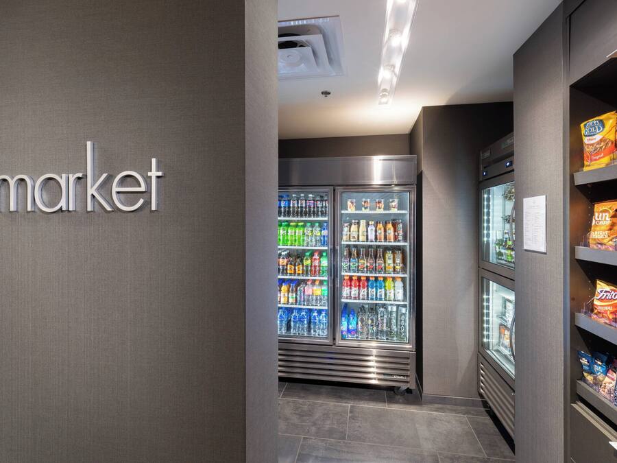 Uma área de máquinas de venda automática com lanches e bebidas, um letreiro com a palavra 'market' e um refrigerador.