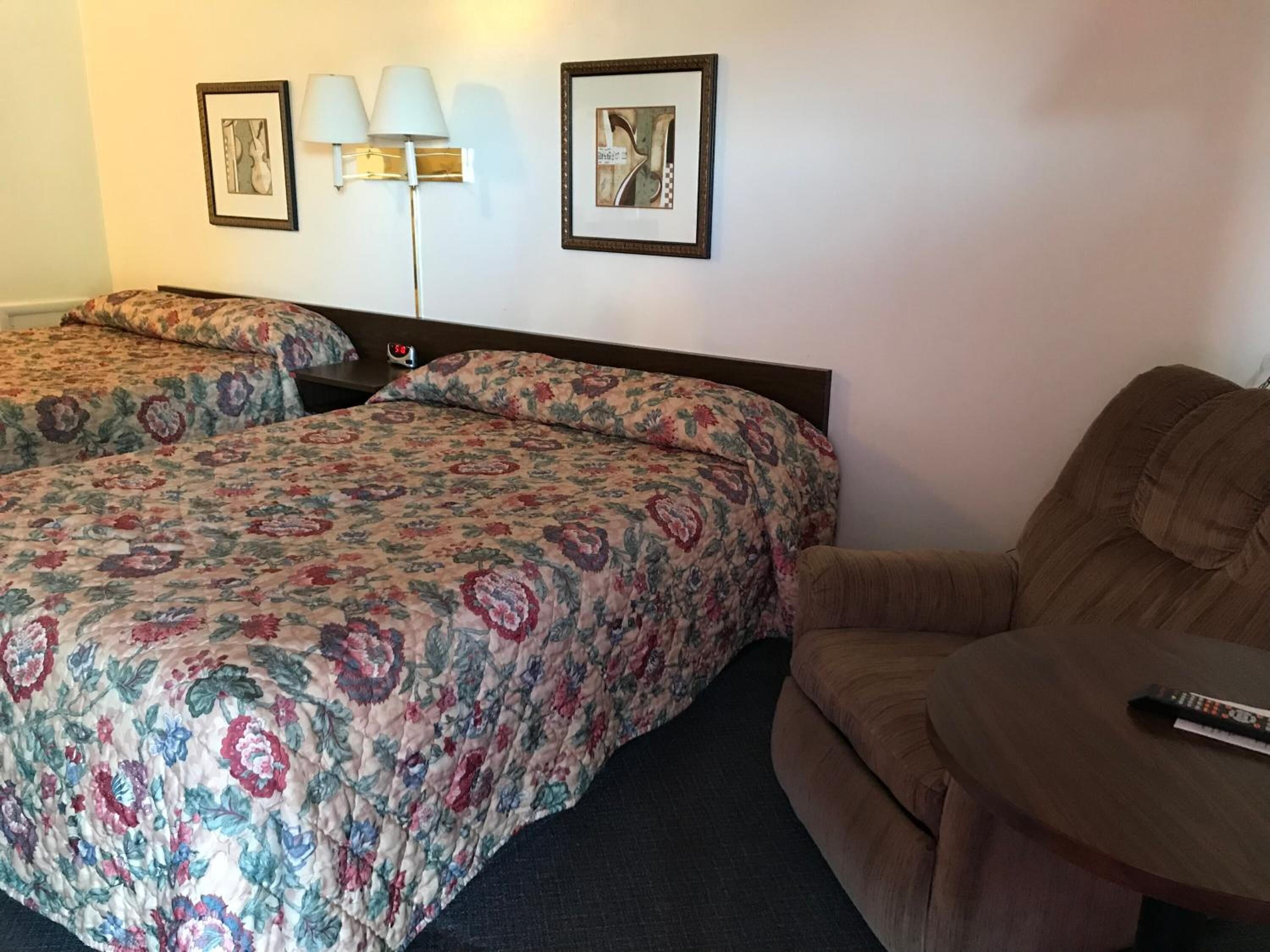 A hotel room with two beds, a sofa, a lamp, and a framed picture on the wall.