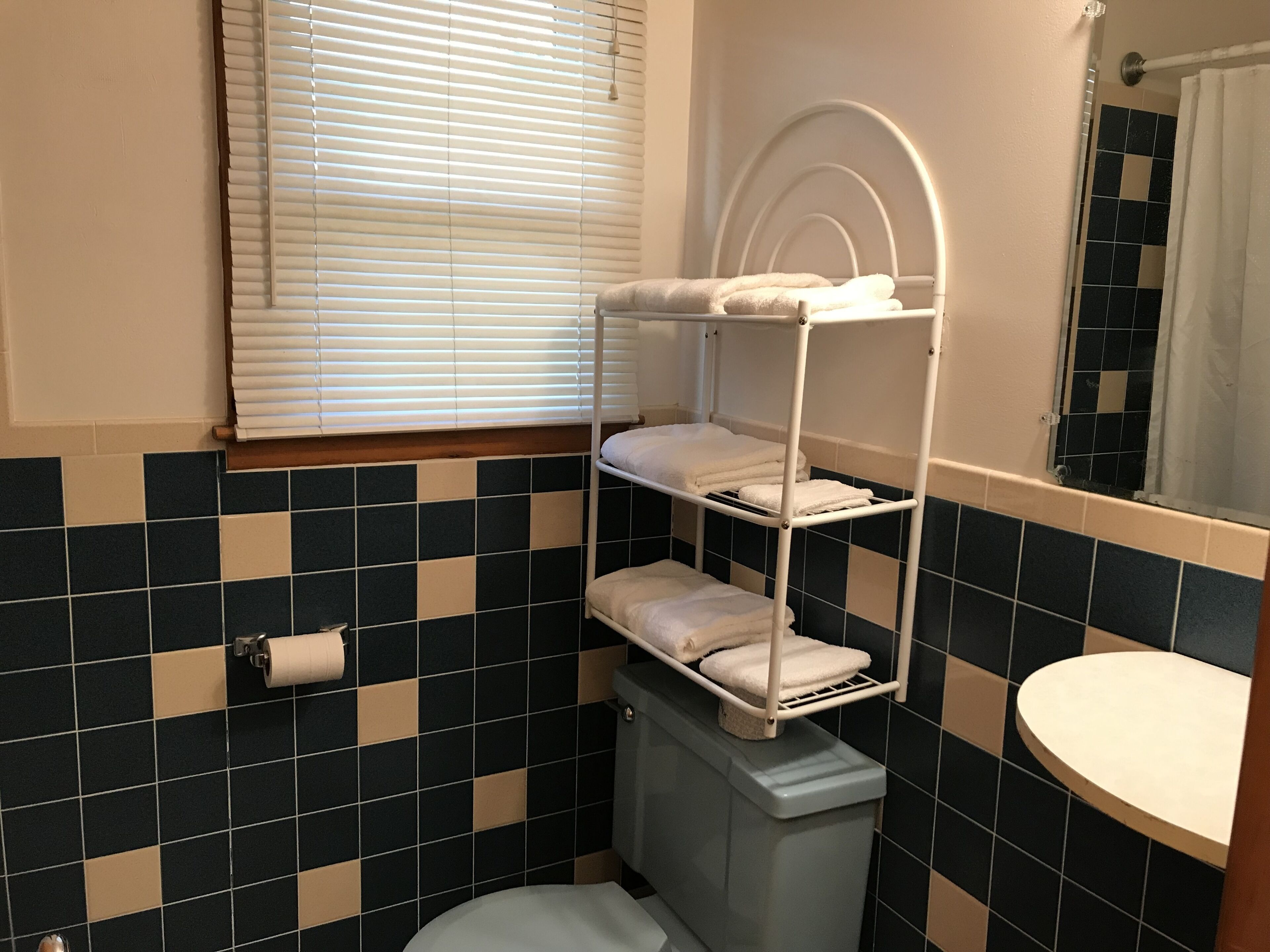 Un baño con piso de baldosas, un inodoro, un lavamanos y una ventana con persianas.