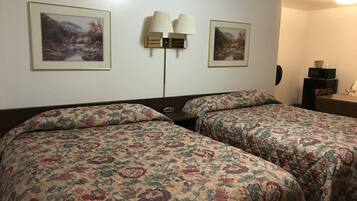 A room with two beds, each with floral bedding, a wall-mounted lamp, and two framed pictures.