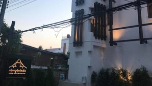 Ein mehrstöckiges Gebäude mit weißer Fassade und dunklen Fensterrahmen, umgeben von Stromleitungen und Grünflächen.