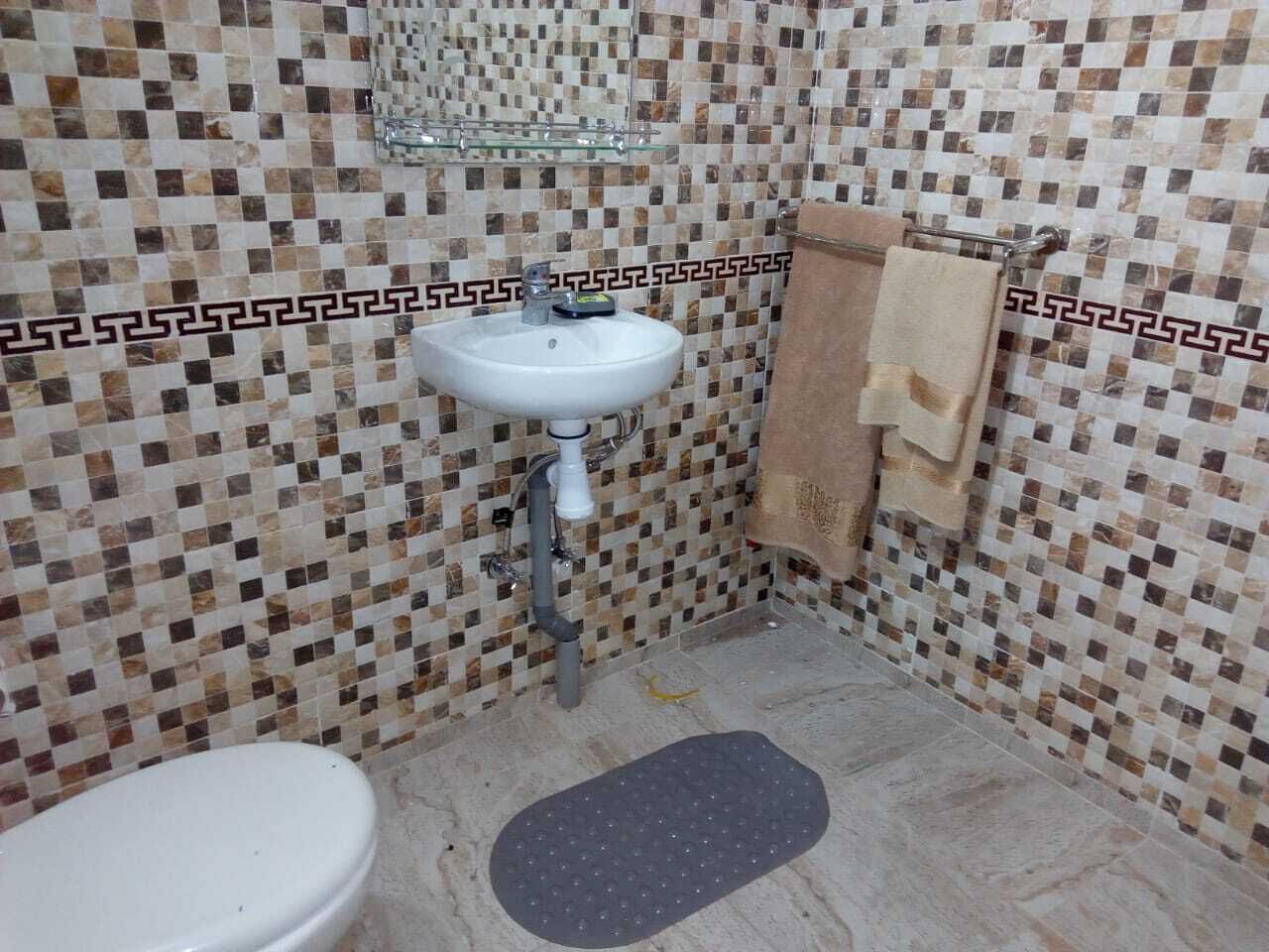 A bathroom with a white sink, tiled walls, and a beige towel hanging on the wall.