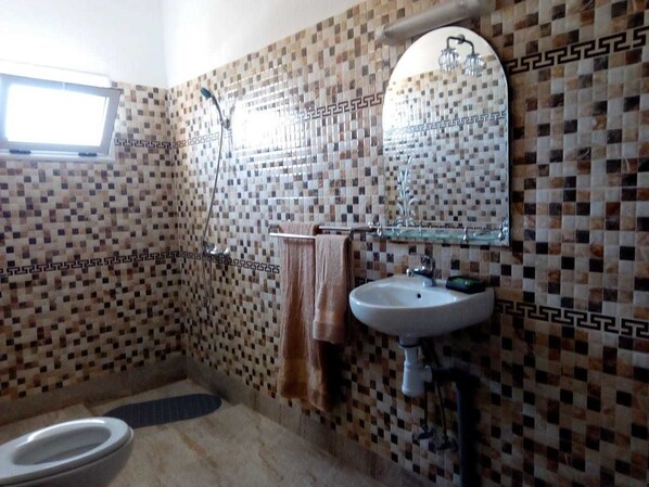 Un baño con paredes de mosaicos, inodoro, lavamanos y ducha.