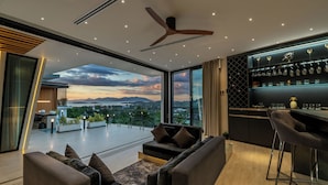 Ein modernes Wohnzimmer mit großem Fenster, Deckenventilator und Barbereich mit Gläsern.