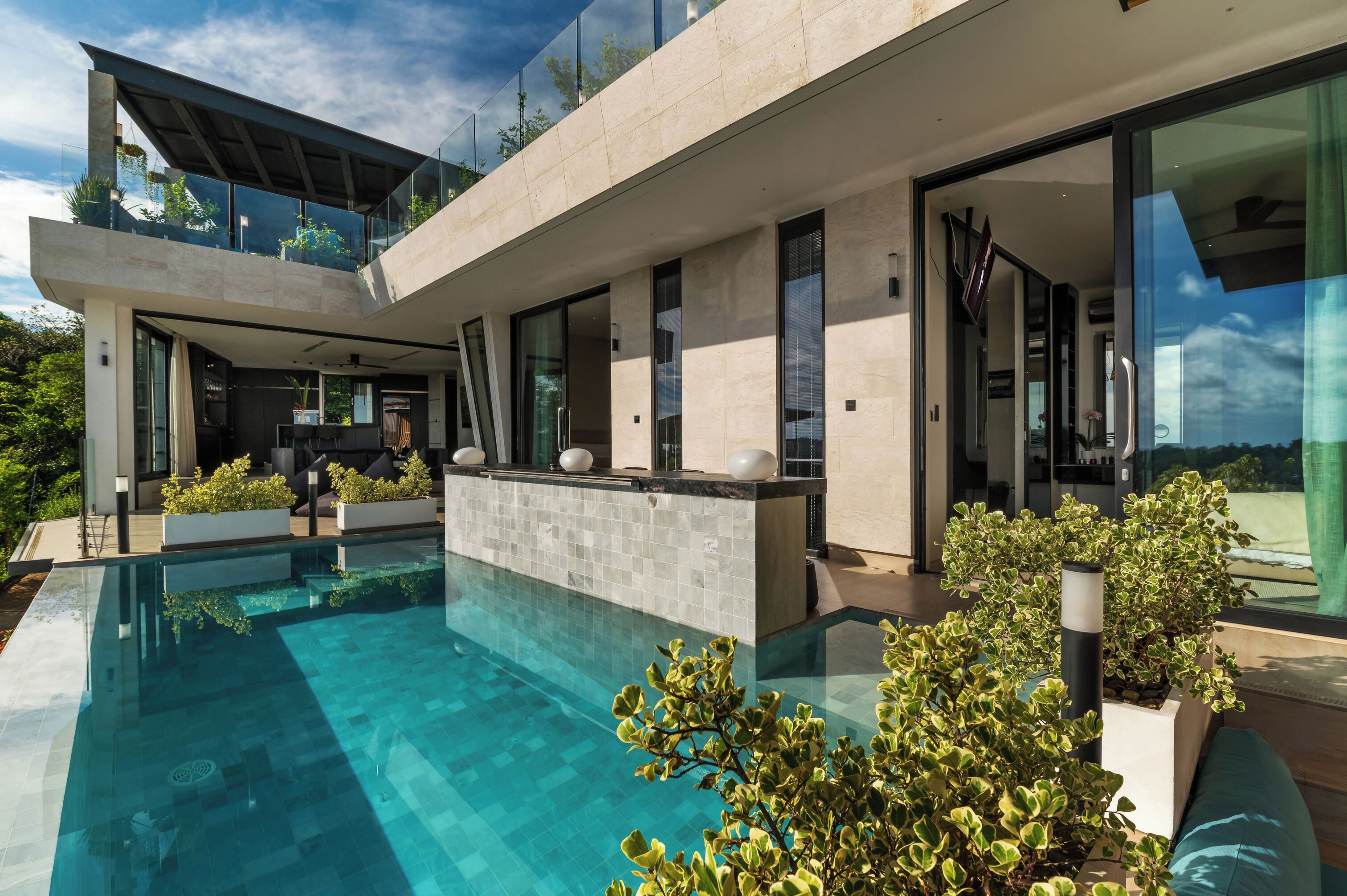 Una casa moderna con piscina, ventanas amplias y un balcón con plantas.