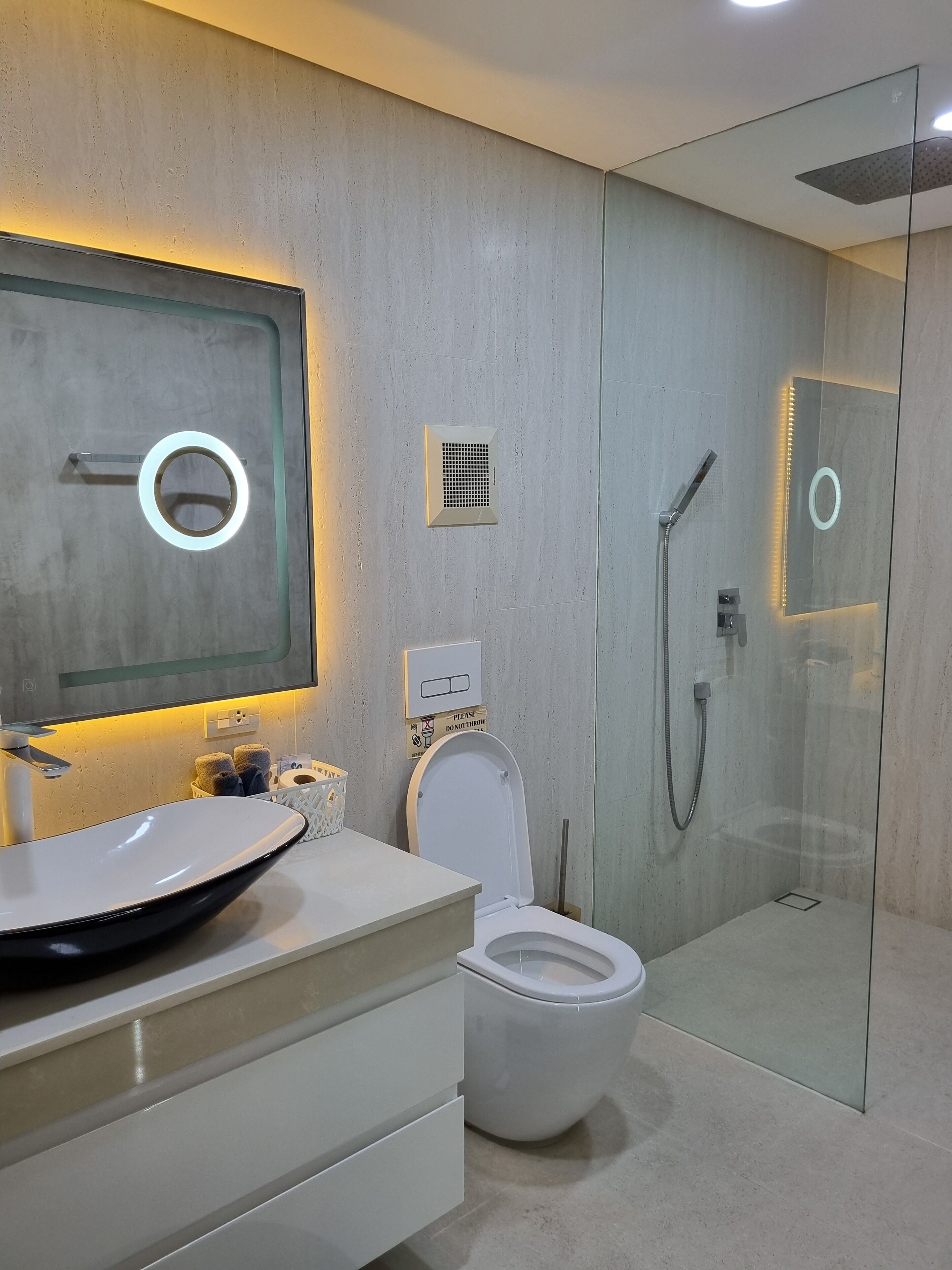 Un baño moderno con ducha envuelta en vidrio, un lavabo blanco con un recipiente amplio y un inodoro con la tapa cerrada.
