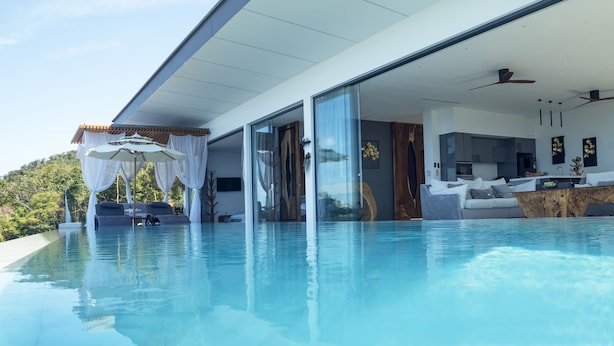 Ein moderner Infinity-Pool mit Glasrand, eine private Außenküche und eine überdachte Lounge-Ecke.