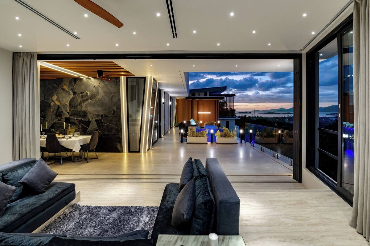 A modern interior with a dining area, a sofa, and a view of the sky.
