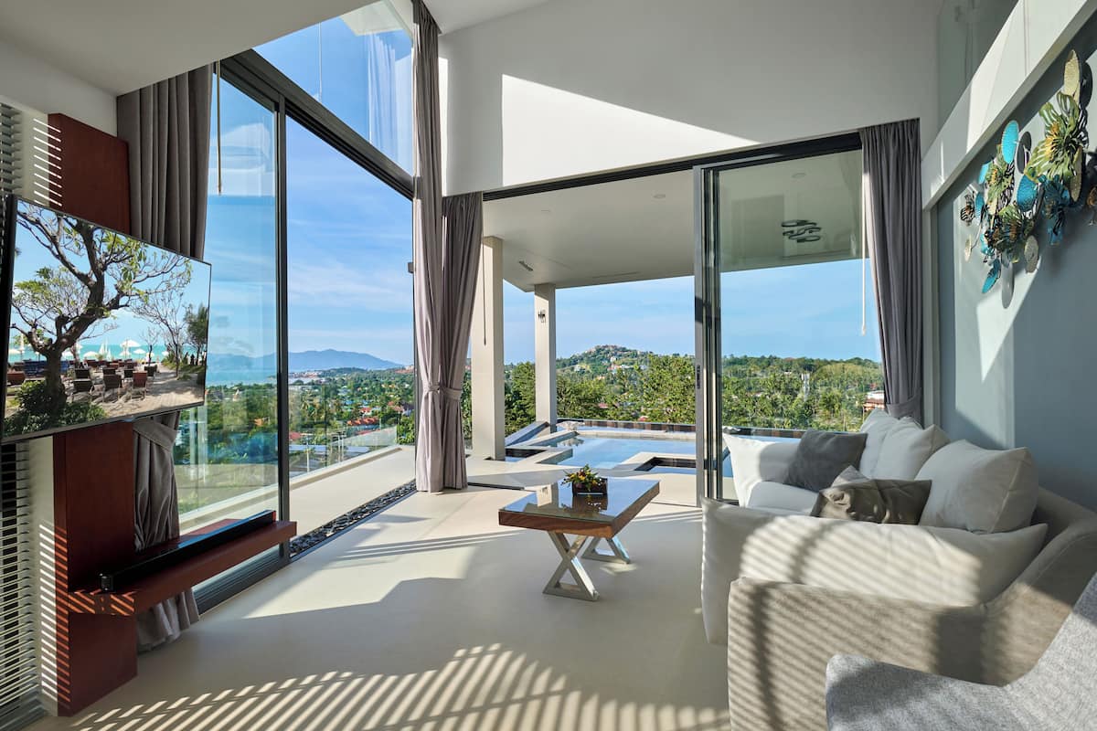 A modern living room with a large glass wall, a flat-screen TV, a sofa, and a coffee table.