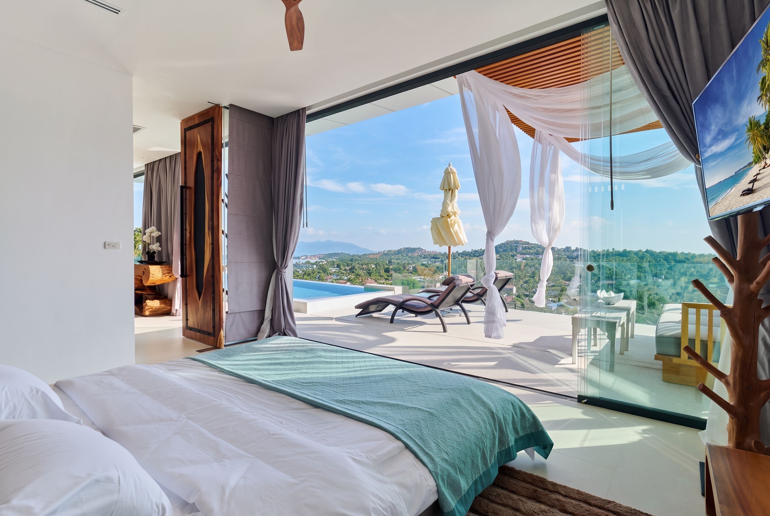 A bedroom with a large bed, a view of a pool and beach, and a sliding glass door leading to an outdoor seating area.