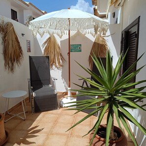 Un petit espace patio avec un parasol blanc, une chaise, une petite table et un pot de fleurs.